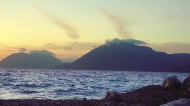 平静的冲浪在卵石沙滩上 美丽的落日掠过海湾 掠过高山 — 图库视频影像