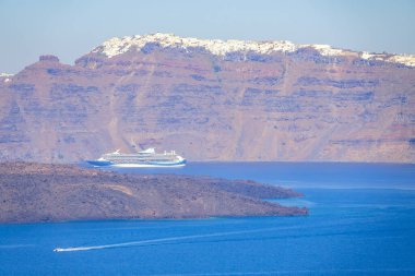 Yunanistan. Santorini 'nin kayalık sahillerinde güneşli bir yaz günü. Büyük yolcu gemisi ve küçük motorlu tekne.