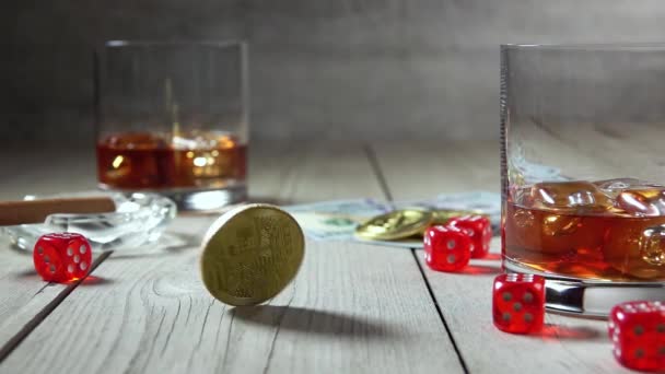 旧木桌威士忌加两杯冰块的威士忌 美元钞票 烟灰缸里的雪茄几个骰子比特币在中间旋转 慢动作 — 图库视频影像