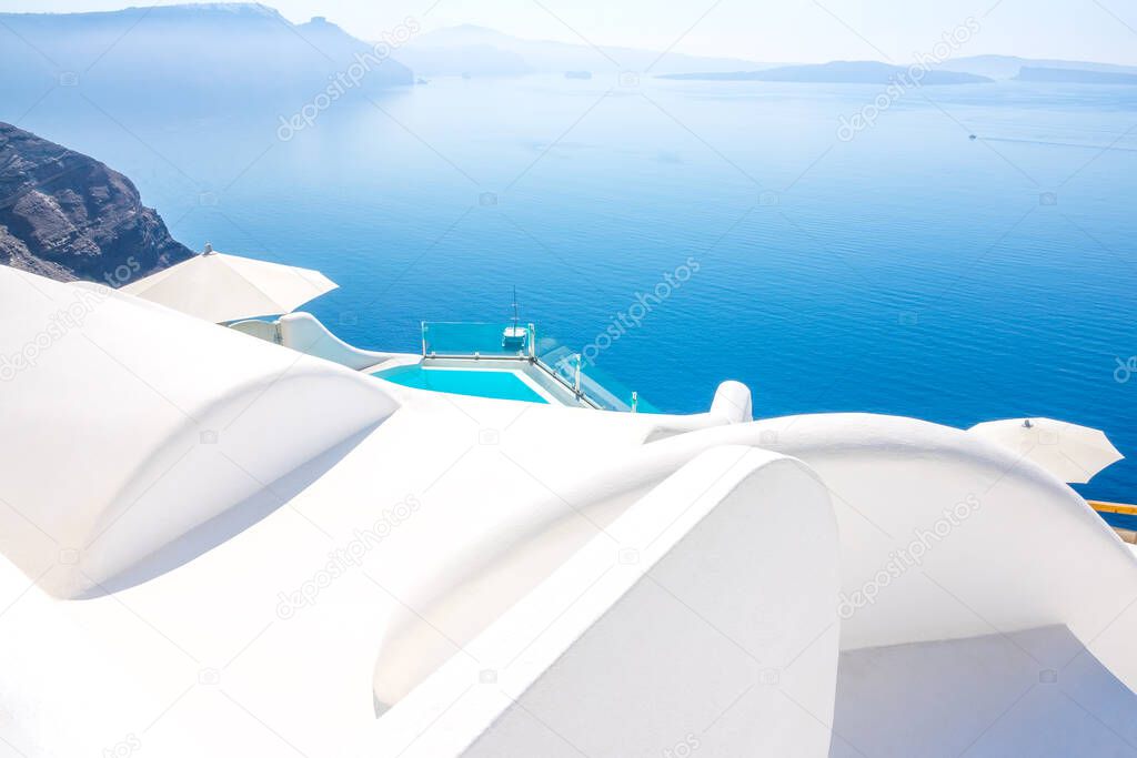 Greece. Sunny summer day on the caldera of Santorini island. Traditional white roofs and the edge of the blue pool with seaview