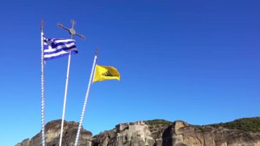 Yunanistan. Meteora 'daki kayalık manastırlarda güneşli ve bulutsuz bir gün. Mavi gökyüzüne karşı bayrak direkleri. Yavaş çekim