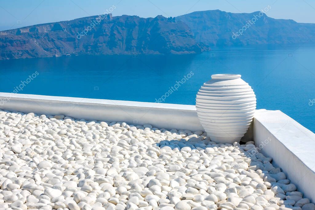 Greece. Sunny day on Santorini. White pebbles and white stone vase. Seascape with rocky islands