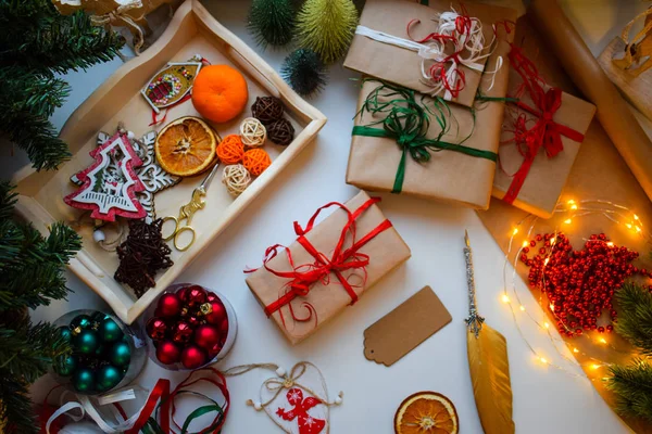 Készül az ünnepekre, keresztkötés ajándék-ban nátronpapír, címkék aláírása, körülvéve karácsonyi apróságok — Stock Fotó