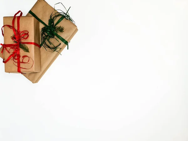 Две рождественские подарочные коробки, упакованные в крафт и красные и зеленые ленты на белом фоне — стоковое фото