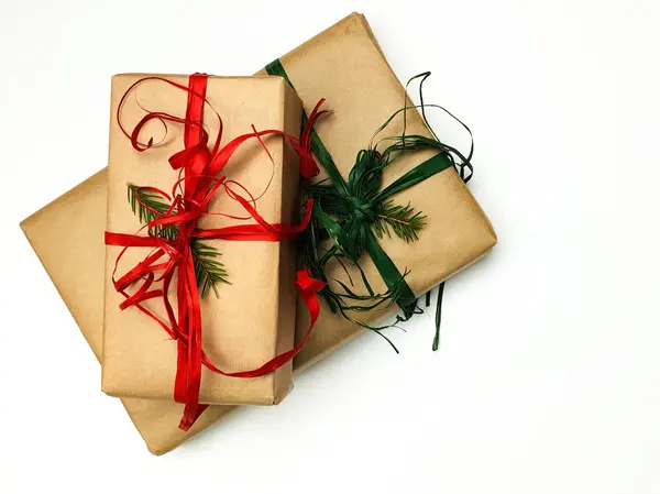 Две рождественские подарочные коробки, упакованные в крафт и красные и зеленые ленты на белом фоне — стоковое фото