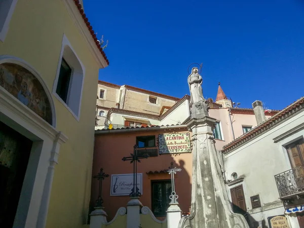 Statue with an arrow next to the catalan center on the background of houses and blue sky on the square in Maratea, Basilicata, Potenza, Italy
