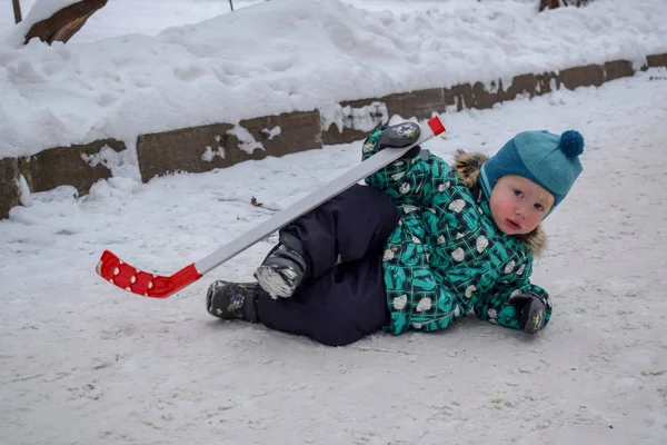 Der kleine Junge war des Eishockeyspiels müde und legte sich im Winter mit einem Stock in einem Park auf den Schnee — Stockfoto