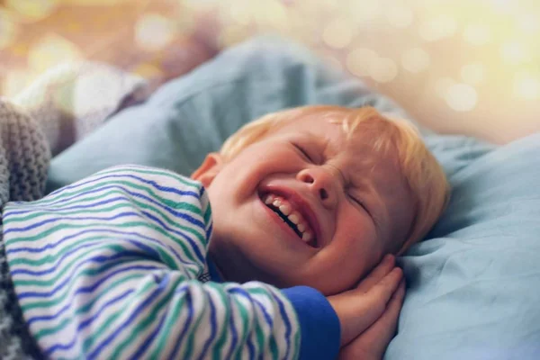 Küçük bir sarışın çocuk yanağını altında elleriyle Çizgili Pijama içinde yanıp söner, uyumaya çalışıyor