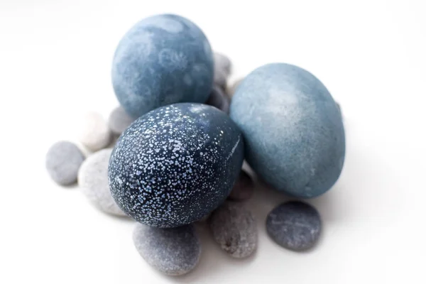Three colored blue, gray marble eggs lie on a white background on stones — Stock Photo, Image