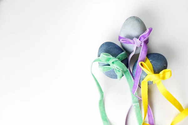 Three colored blue, gray marble eggs tied with multicolored green, purple, yellow ribbons on a white background — Stock Photo, Image