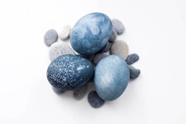 Três ovos de mármore azul, cinza coloridos jazem sobre as pedras em um fundo branco — Fotografia de Stock