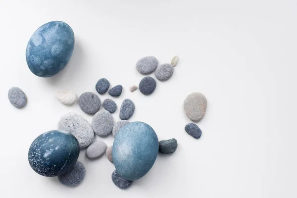 Three colored blue, gray marble eggs lie on a white background among the stones — Stock Photo, Image