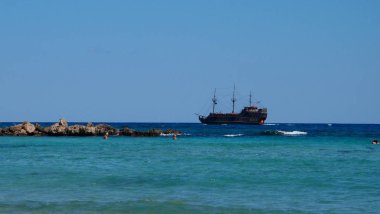 Beyaz kuzu ve kayalar ile turkuaz mavidenizde yüzen, bir korsan gemisi olarak stilize