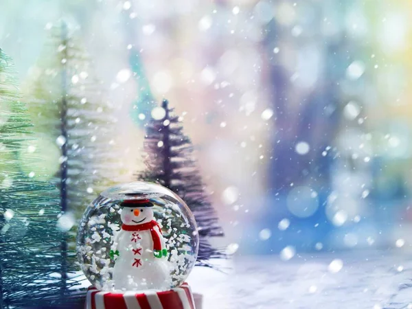 Улыбающийся снеговик в снежном шаре на фоне рождественских елок, боке и снежинок . — стоковое фото