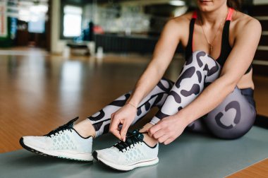Çekici sporcumuz spor salonunda ayakkabı bağcığı bağlama. Kız bir mat fitness için hazırlanıyor. Spor eğitim kavramı. Yan görünüm.
