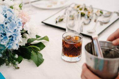 Eller buzlu viski için bir barmen de bar, Restoran, dostum. Bir bardak viski, viski rustik bir festival tablo kopya alanı içinde belgili tanımlık geçmiş buz küpleri ile. Portre, içecekler.