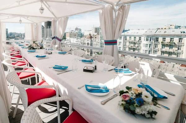 A rooftop restaurant overlooking the city. Festive table served dishes and decorated with flowers for wedding party. Image of celebrate outdoor party on background town.