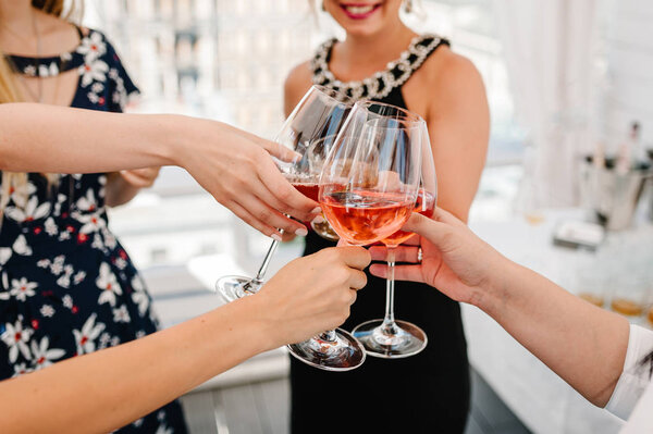 Cheers! People celebrate and raise glasses of wine for toast. Group of man and woman cheering with sparkling champagne in rooftop restaurant overlooking the city.