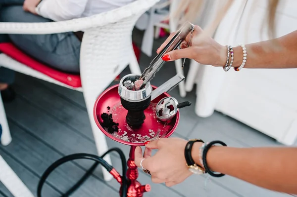 Kadın forseps shisha nargile için tutan eller ve metal kabın içinde sıcak kömürleri ayarlar. Kırmızı nargile iç restoranda ahşap zemin üzerinde duruyor. Sigara kavramı. Geleneksel Asya gevşeme.
