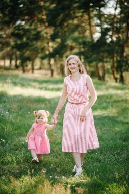 Annesi bir kızı ile çalışır ve yaz gününde, tatil doğa üzerinde elini tutar. Anne ve kız yürüyüş ve gün batımı anda parkta oynamak. Dostu aile kavramı. Yakın çekim.