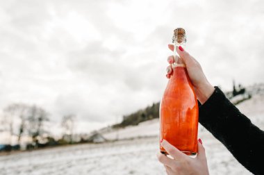 Kadın bir şişe şampanya kış dağlar arka planı-tamam. Doğada karlı bir yürüyüş. Seyahat ve tatil kavramı. Tatil kış sezonu.