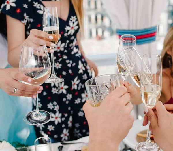 Cheers! People celebrate and raise glasses of wine for toast. Group of man and woman cheering with sparkling champagne and whiskey, scotch, whisky, brandy in rooftop restaurant overlooking the city.