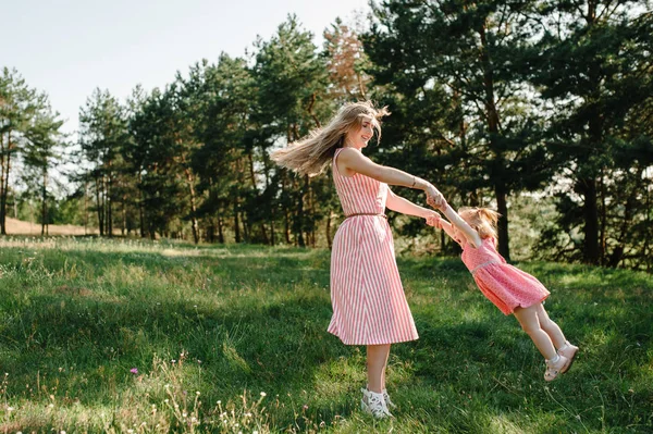 若い母親は緑の春パークで手に娘を回転 — ストック写真