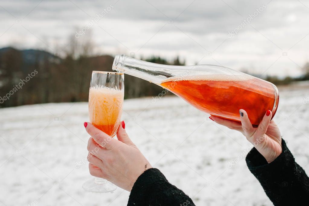 Close view of woman hands pouring champagne into glass on winter mountains background