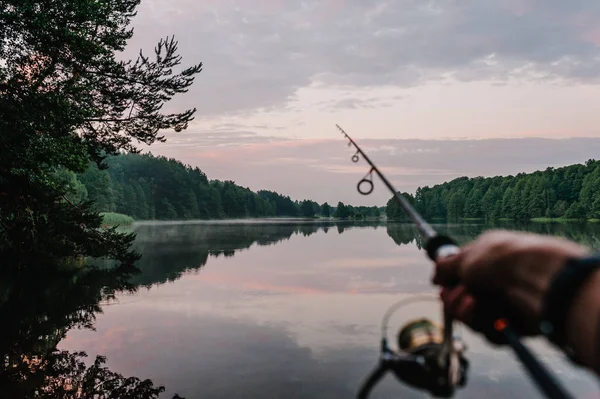 日落时在河岸上用鱼竿旋转卷轴的渔民的近景 — 图库照片