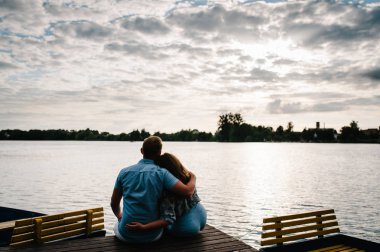Romantik erkek ve iskelede oturup ve çarpıcı günbatımı zevk kadın arkadan görünüş