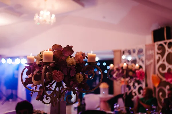 composition of flowers and burning candle on festive table at wedding banquet hall