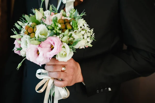 Bridal bouquet with gentle pastel flowers and pink roses and greenery in groom hand