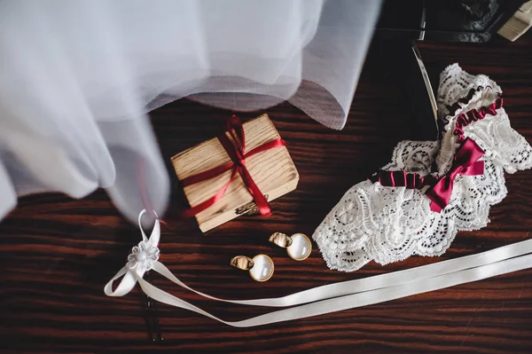 Elegant earrings, wooden box and garter on brown table