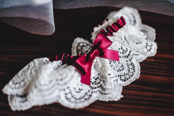 white wedding garter with red bow on brown table
