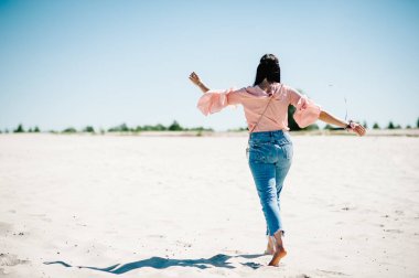 Doğada kumlu plajda yürüyüş yandan arkadan görünüm çiçek yaka çiçeği ile şık seksi genç kızın. Parti boho tarzı. Hen-partiler akşam kızlık. 