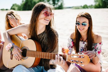 Şampanya içmek ve kumlu plaj, bekarlığa veda partisi boho tarzı üzerinde otururken gitar çalmak güzel mutlu ince şık seksi genç kız 
