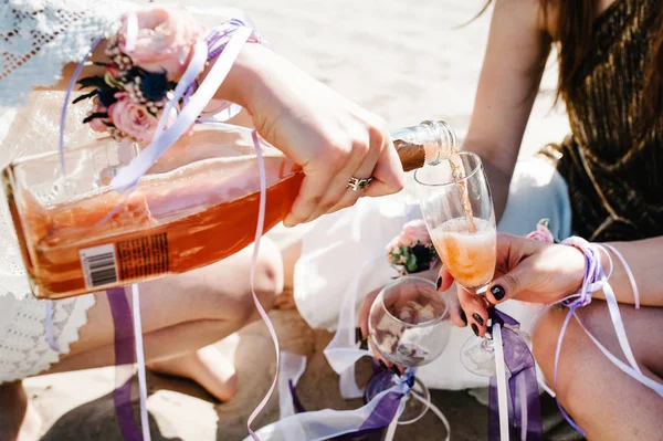 Kızlar, kumlu plaj halı üzerinde otururken şampanya cam içine dökme bachelorette parti boho tarzında 