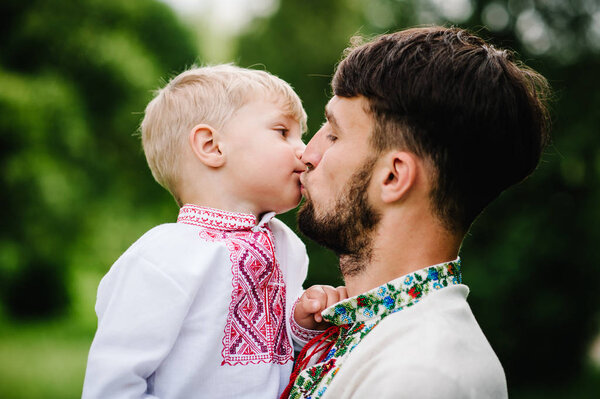 Happy little boy with dad in embroidered shirt having fun in park