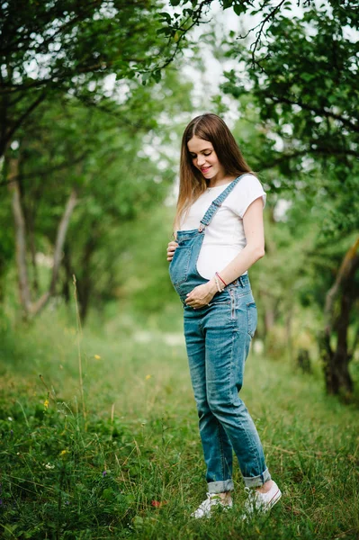年轻的怀孕快乐的女人走在绿色的避暑公园 — 图库照片