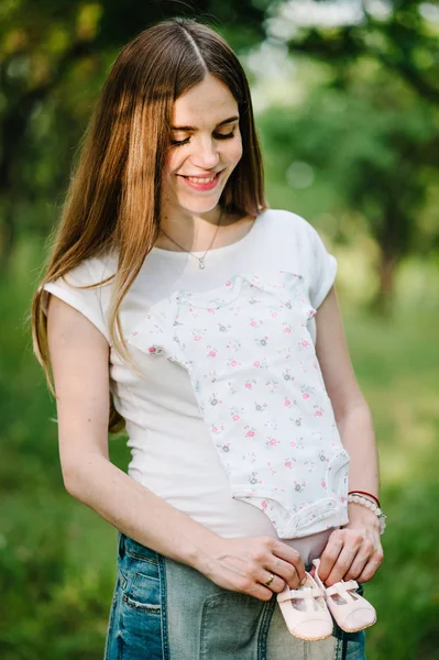 Grávida Feliz Jovem Segurando Sapatos Bebê Roupas Estômago — Fotografia de Stock