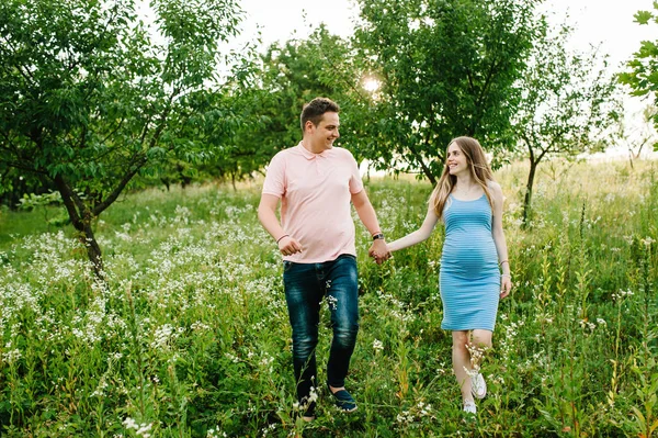 妊娠中の女性と夫が緑の暖かい夏の森の中を歩く — ストック写真