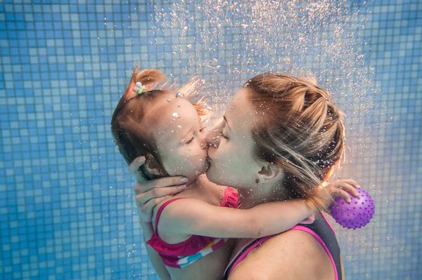 Young mother teaching daughter to swim underwater with in pool
