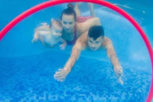 Young mother and father teaching son to swim on swimming lesson underwater with pool
