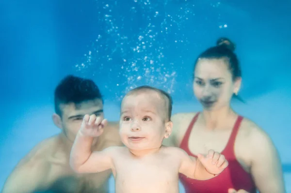 プールで水中で水泳のレッスンを泳ぐために若い母親と父親の教えの息子 — ストック写真