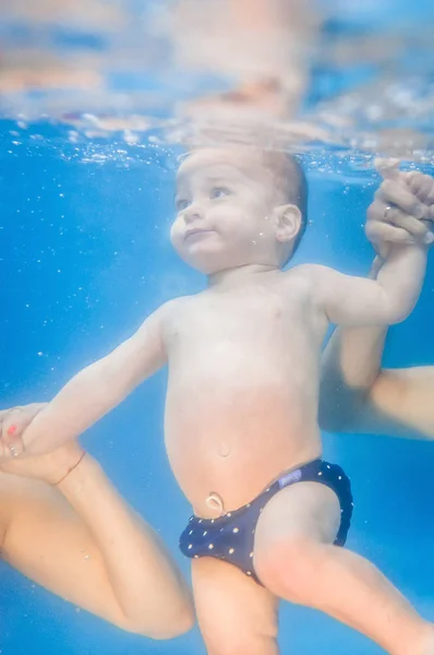 プールで水中で水泳のレッスンを泳ぐために若い母親と父親の教えの息子 — ストック写真