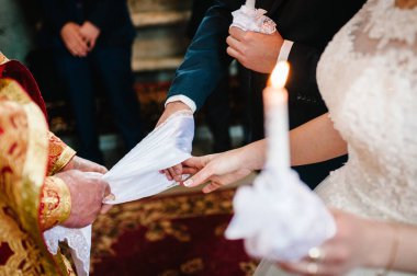 Gelin ve damadın elleri düğün havlularını bağladı. Rahip gelinin el havlusunu bağlar. Kilisedeki genç çiftlerin elleri. Kilise töreninde el ele tutuşan çift. Düğün günü..