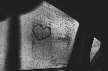 Yağmurdan sonra ıslak arabanın camına kalp çizildi. Kapatın. Siyah beyaz fotoğraf