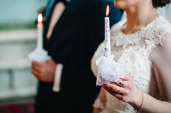 The bride holds a wedding candle with a blue bow. Burn candle. Spiritual couple, groom. holding candles during wedding ceremony in christian church. close up.