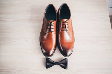 Süslü düğün kahverengi erkek ayakkabıları, bir kelebek ışık masasında yatıyor. Beyaz arka plan. Aksesuarlar damat.