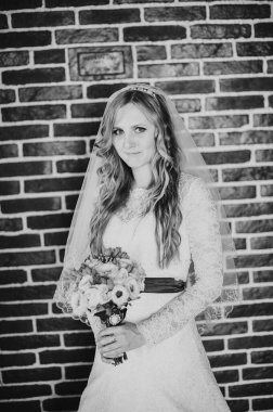 Bir buket çiçek standı ve poz veren görkemli zarif bir gelin. Tuğla duvarın arkasında. Kapatın. Siyah beyaz fotoğraf. Portre.